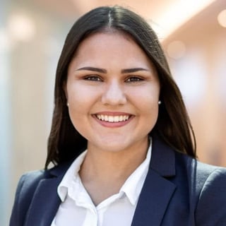 Professional headshot of a smiling woman with long dark hair wearing a dark blazer and white shirt