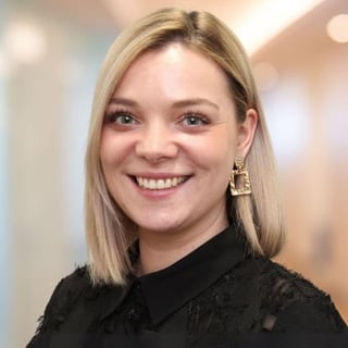 Smiling woman with shoulder-length blonde hair wearing a black lace top and gold earrings