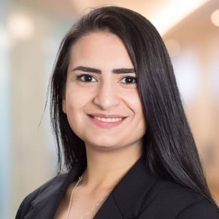 Professional headshot of a smiling woman with long black hair and pink lipstick wearing a black blazer