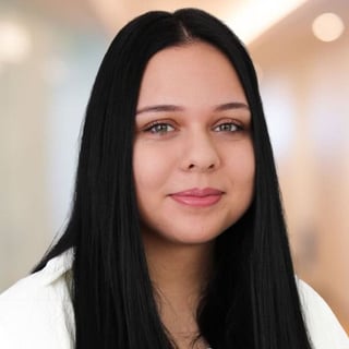 Portrait of a woman with long black hair and pink lipstick against a blurred neutral background